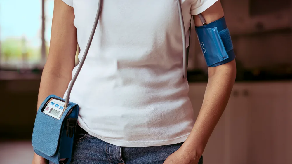 Person wearing a 24-hour ambulatory blood pressure monitor, cuff on the upper arm and recorder at the waist