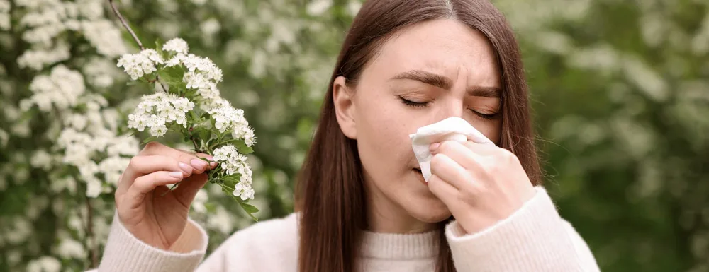 Woman sneezing into a tissue beside a tree in blossom