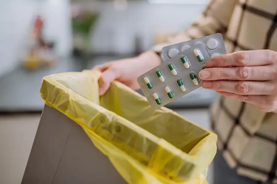 Unused blister pack of tablets being dropped into a household bin