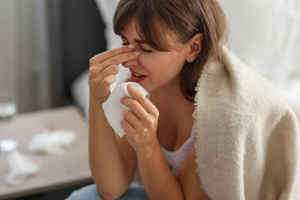 Woman pinching the bridge of her nose with sinus pain, holding a tissue